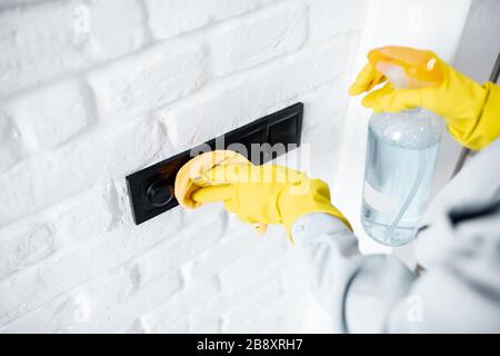 Woman in protective gloves disinfecting wall switches while cleaning at home, close-up view on hands Stock Photo
