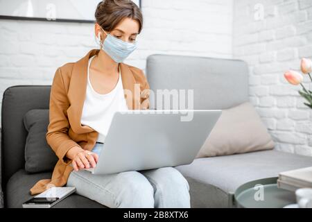 Woman in medical mask working on laptop online from home. Stay at home during a virus pandemic concept Stock Photo