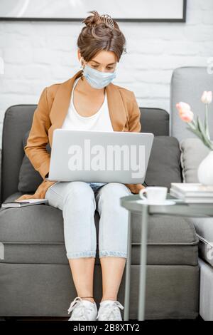 Woman in medical mask working on laptop online from home. Stay at home during a virus pandemic concept Stock Photo