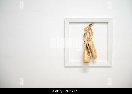 Sofia - March 3, 2020: old ballerina shoes hung in a frame on a white wall, as a memory of a ballerina's career Stock Photo