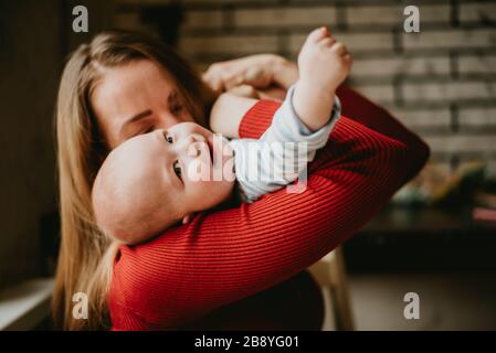 A mom holds a child in her arms. A mother kisses a toddler. A young women hugs her infant. A girl has fun and rejoices with the baby. Stock Photo