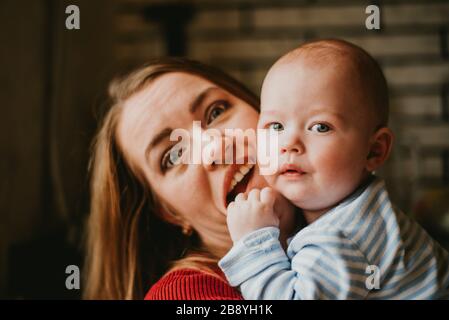 A mom holds a baby in her arms. Mother hugs her toddler. A young woman has fun and rejoices with the child. A girl clutches a infant.Close up. Stock Photo