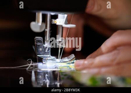 Seamstress sewing cloth on a sewing machine, working by the light of the built-in hardware lamp. Steel needle with looper close-up. Stock Photo