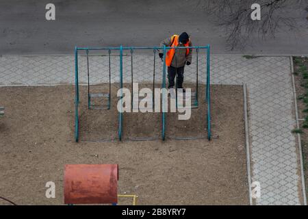 An unidentified man in a protective suit sprays a children's swing with antiviral drugs. covid-19 endemic Stock Photo