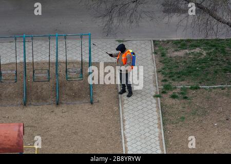 An unidentified man in a protective suit sprays a children's swing with antiviral drugs. covid-19 endemic Stock Photo