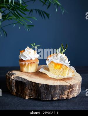 Homemade lemon cupcakes decorated with lemon and leaves on dark blue background.
