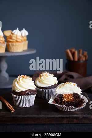 Chocolate cupcakes with peanuts and caramel decorated with cream on dark background. Carrot cupcakes with caramel nearby. Free space for your text Stock Photo