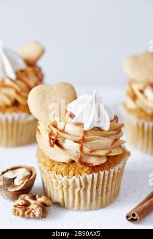 Carrot cupcakes with walnuts and spices decorated with biscuit, meringue and salty caramel on white background. Free space for your text Stock Photo
