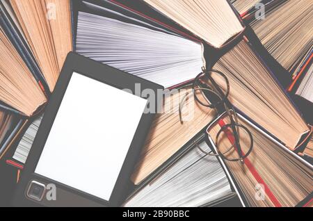 The e-book with a white screen lies on the open multi-colored books that lie on a dark background, close-up Stock Photo