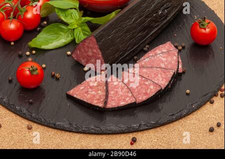 sliced smoked sausage with sauce, cherry tomatoes and basil on a black graphite board. top view Stock Photo