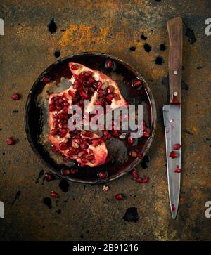 Overhead image of a split pomegranate on a metal plate with a knife on a rusty metal background Stock Photo