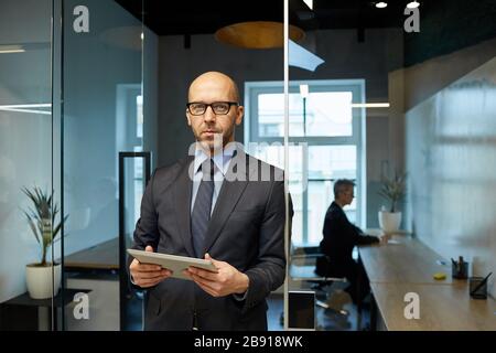 Waist up portrait of successful bald businessman standing in modern office interior holding tablet, copy space Stock Photo