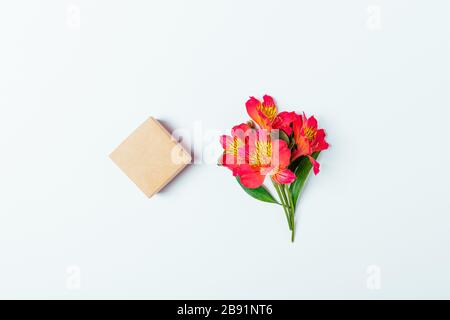 Blank gift box made of brown eco paper next to small bunch of fresh flowers on white background, top view. Stock Photo
