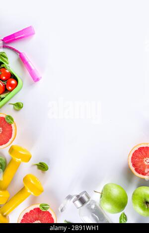 Fitness and healthy food lifestyle concept. Dumbbells, diet fruit and vegetable lunch box, water and jump rope on white background. Flatlay image, top Stock Photo