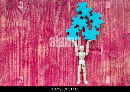 Wooden doll holding pieces of jigsaw puzzle. Solutions and challenges concept. Stock Photo