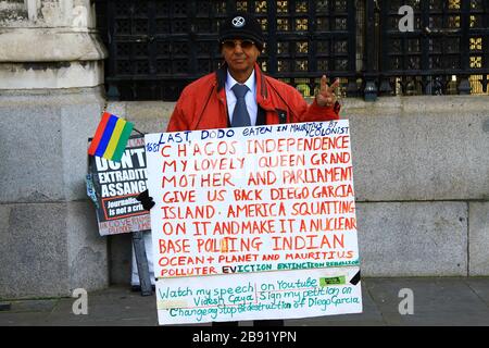 A man protests outside the gates of the British parliament building [ House of Commons entrance ] about the destruction of the island of Diego Garcia [ British Indian ocean territory ]. He is concerned that the United States and United Kingdom joint military base is destroying the Island and surrounding environment. His is holding  a board with words denoting his concerns. Stock Photo