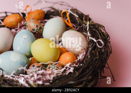 Samara Russia - 03.01.2020: A nest of twigs and hay and a pink paper filler with pastel colored Easter eggs. Painted and decorative eggs for a light Easter holiday. Easter card on a pink background. Stock Photo