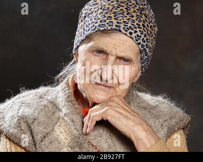 Close up portrait of old woman with thoughtful look on dark background. People of such ages are most vulnerable during epidemics. Stock Photo
