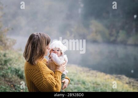 A woman is holding a baby near a river