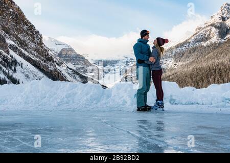 Young Couple Skating Together on Frozen Lake Louise in Winter Stock Photo