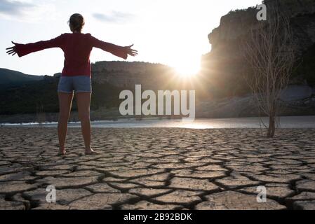 Backlit woman at the edge of a lake with her arms outstretched. Stock Photo