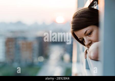 Young sad woman looking outside through balcony of an apartment building Stock Photo