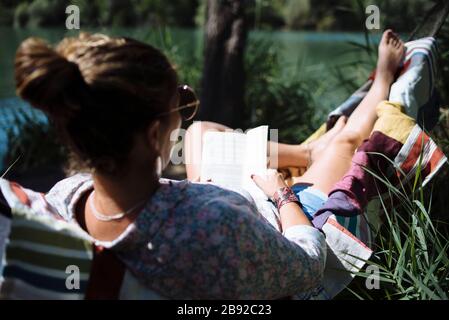 Woman with sunglasses reading a book lying on a hammock. Stock Photo