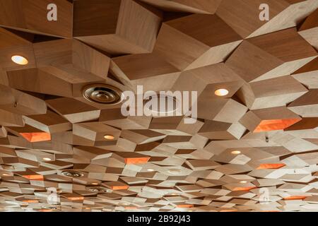 Lights Speakers Ventilation and Fire Sprinklers on Drop Ceiling Wooden Texture Tiles. Hexagon Metal Timber Panels. Three Dimensional Cube Shape Decora Stock Photo