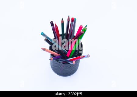 Bunch of different colored pen and pencil crayons gathered in a black pencil holder on a white background Stock Photo
