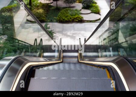 Blurred Not in Focus Landscaped Courtyard on the Background. Escalator Going Down to the Green Sunken Plaza. Technology and Nature. Stock Photo