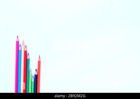 Eight different colored pencil crayons gathered in a wave saved row on a corner of a white background Stock Photo