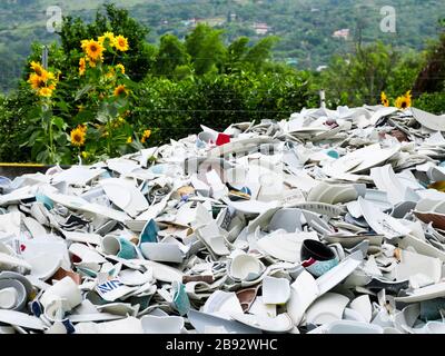 pile of broken china ready to be recycled and used as raw material for construction bricks with a garden of sunflowers on the background Stock Photo