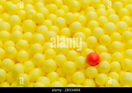 Coloured yellow & red small polystyrene balls. Conceptual for Covid-19 self-isolation, disease carrier, infected person, isolated, lost in the crowd. Stock Photo