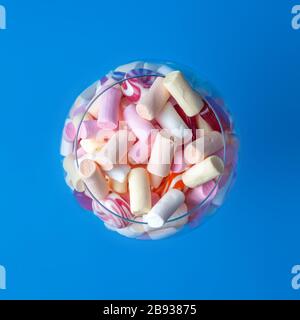 Mini marshmallows in a glass on a blue background. Multi-colored marshmallows in a wine glass. View from above. Copy space. Close-up Stock Photo