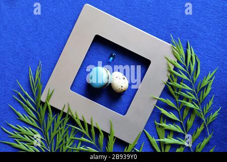 On a blue trendy background, eggs in a gray, silver frame. Green leaves of tropical plants. Trendy color background. Close up. Copy space Stock Photo