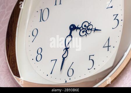 A modern wall clock with a white dial hangs on the wall Stock Photo