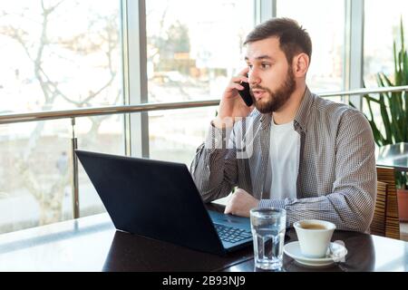 Phone conversation. Upset young man talking over phone disappointed hear bad news. Portrait tired, exhausted man in cafe or modern office with Stock Photo