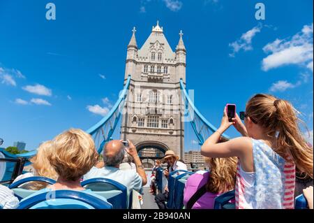 Tourists on open top double decker Original London Sightseeing Tour bus crossing Tower Bridge, London, UK Stock Photo