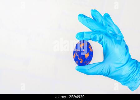 Easter time in quarantine concept. Female hand in blue medical gloves holding Easter eggs. Concept of Easter holyday and spring break during Stock Photo