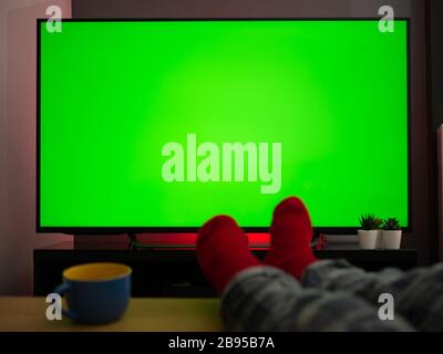 feet up on the table in front of green screen tv televison chroma key at home Stock Photo