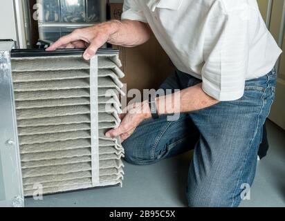 Senior caucasian man changing a folded dirty air filter in the HVAC furnace system in basement of home Stock Photo