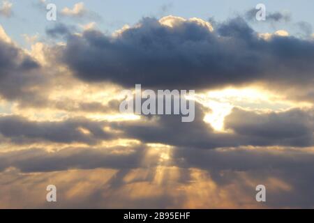 The sun at sunset or dawn behind the clouds, shines through. The sun's rays in the sky. Stock Photo