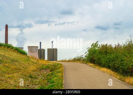 View across meadows, pathway and bushes to a power plant with steaming cooling tower on the horizon Stock Photo