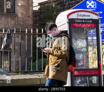 An asian male checks his smartphone while wearing a mask as protection against covid-19 on a Newcastle upon Tyne street, UK, during the 2020 pandemic. Stock Photo