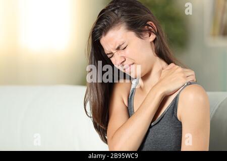 Girl complaining suffering shoulder ache sitting on a couch in the living room at home Stock Photo