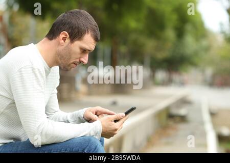 Side view of serious adult man using smart phone alone in a park Stock Photo