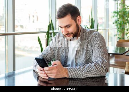 Smart phone texting. Attractive bearded caucasian businessman using smartphone while sitting in office. Businessman using mobile phone app in urban Stock Photo