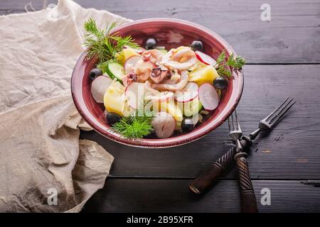 Rustic salad with octopus tentacles, boiled potatoes, cucumbers, fresh radishes, olives and dill. Stock Photo