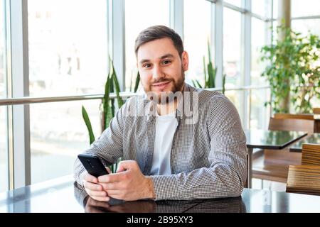 Smart phone texting. Attractive bearded caucasian businessman using smartphone while sitting in office. Businessman using mobile phone app in urban Stock Photo