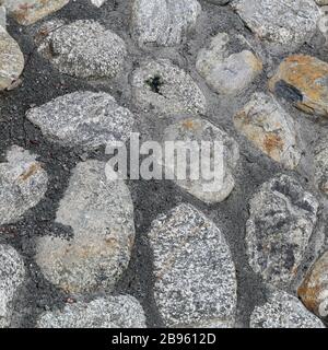 Road made of cobblestones and cement. Grey outdoor floor in a closeup from above. Sidewalk stones are asymmetrical and most of them have grey stones. Stock Photo